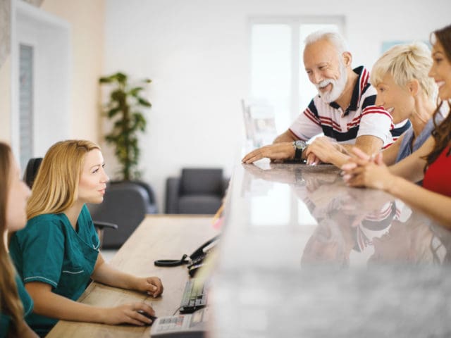 A group of people waiting at a counter talking to a nurse