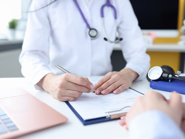 A doctor is writing on a clipboard with a pen while someone sits in front of her