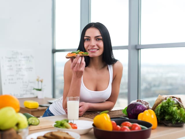A woman is eating a piece of toast and drinking a glass of milk
