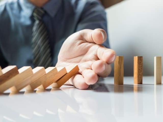 A man's hand is stopping a row of wooden blocks from falling